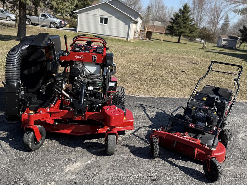 Our stand-on mower with a bagging system, beside our walk-behind mower
